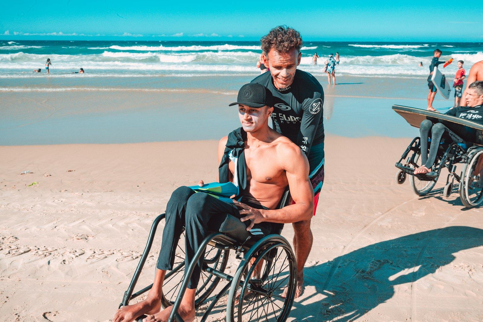 Young man in a wheelchair on the beach with a friend