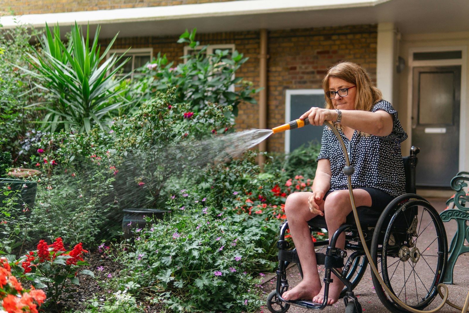 Woman in a wheelchair watering plants in her garden