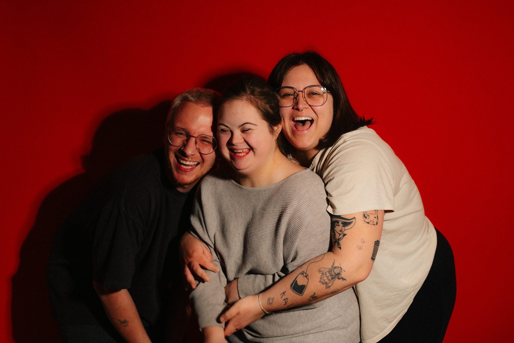A young woman with Down syndrome laughing and hugging with two friends