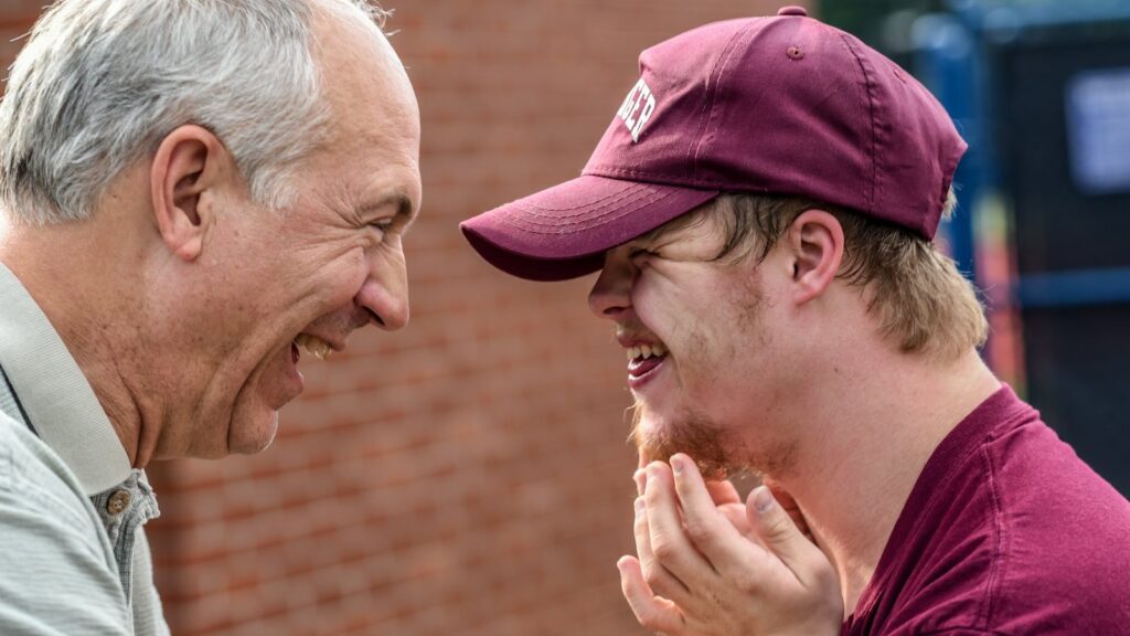 A young man with Down syndrome and an older man laughing together