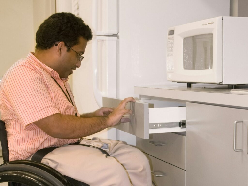 A man in a wheelchair opening a low kitchen drawer in an accessible kitchen