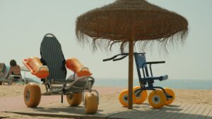 Two beach wheelchairs with large sand wheels under a straw umbrella on the sand