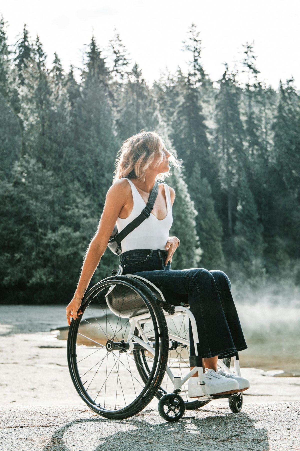 Young woman in a wheelchair smiling outdoors among tall trees
